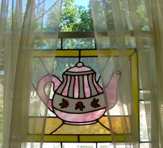 a stained glass window with a pink teapot on it's side and trees in the background