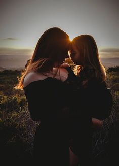 two women are standing in the grass with their backs to each other as the sun sets behind them