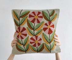 two hands holding up a decorative pillow that has flowers on it and leaves in the middle