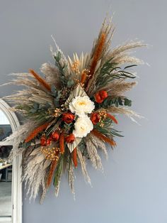 an arrangement of dried flowers and foliage hangs on the wall in front of a mirror