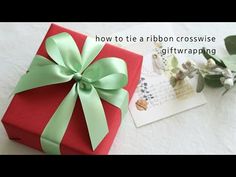 a red gift box with a green bow on it sitting next to a card and flowers