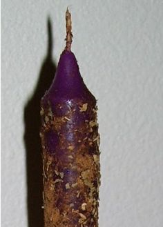 a purple candle that has some kind of substance on it's end and is next to a white wall