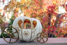 a white pumpkin shaped like a carriage with gold trimmings and wheels, sitting on a ledge