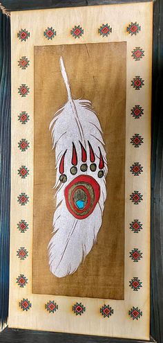 an art piece is hanging on a wooden frame with beads and feathers painted on it