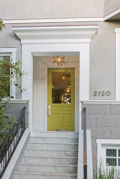 a yellow door is on the side of a gray and white house with steps leading up to it