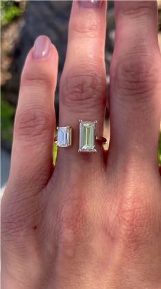 a woman's hand with an emerald and diamond ring on her left hand, in front of the camera