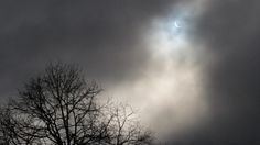 the sun is shining through some clouds in the dark sky above tree branches with no leaves on them