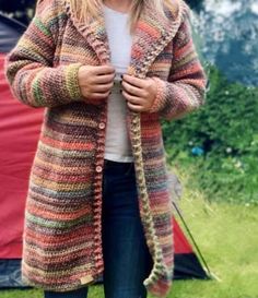 a woman standing in front of a tent wearing a multicolored knitted cardigan