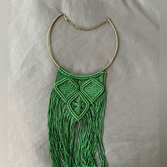 a green necklace with gold chains and fringes on it's end, sitting on a white sheet