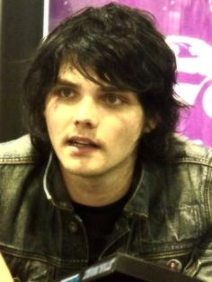 a man with black hair wearing a leather jacket and headphones in front of a microphone