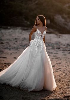 a woman standing on top of a sandy beach wearing a wedding dress with white flowers