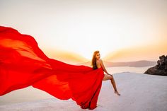 a woman in a red dress is posing on a hill with her long flowing fabric