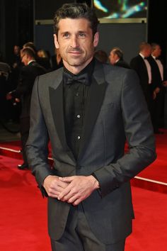 a man in a tuxedo standing on a red carpet with his hands in his pockets