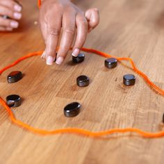 a child playing with an orange string and some black rocks on a wooden table in front of them