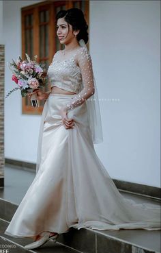 a woman in a wedding dress is standing on some steps and holding a flower bouquet