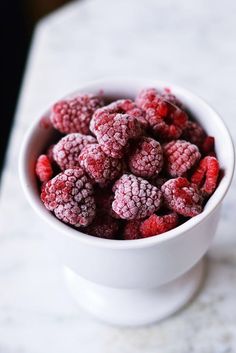 a white bowl filled with raspberries sitting on top of a marble countertop