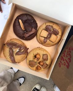 a box filled with assorted cookies on top of a floor next to someone's feet