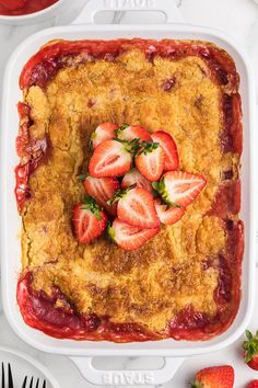 a casserole dish with strawberries in it on a white table next to utensils