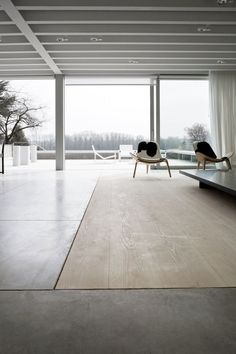 an empty living room with two chairs and a table in front of large glass windows