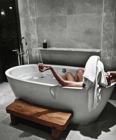 a woman laying in a bathtub with a glass of wine next to her feet