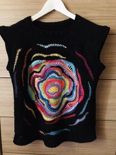 a black sweater with multicolored crochet on it hanging from a hanger