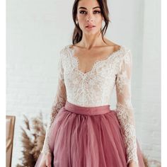 a woman wearing a dress with long sleeves and a pink tulle skirt, standing in front of a white brick wall