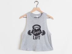 "Live Love Lift workout crop top for women Welcome to StileVybe Tee Co.! This listing is for ONE (1) super soft gym crop tank top that features our \"Live love lift\" fitness design, printed on the front with high quality screen printed heat transfers. * Cotton/Poly blend * Crew Neck * Cropped style * Premium soft feel, not the stiff feeling shirts DESIGN COLOR: BLACK All of the apparel in our shop is printed by hand with love in our home in Massachusetts <3 See photos for sizing and production Sleeveless Sports Crop Top With Letter Print, Sleeveless Letter Print Crop Top For Sports, Cotton Crop Top Activewear For Gym, Sporty Crop Top With Letter Print For Workout, Athleisure Letter Print Crop Top For Gym, Gray Graphic Print Activewear For Workout, Funny Gym Shirt, Lift Workout, Crossfit Shirts