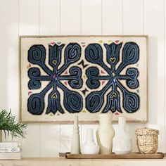 a blue and white wall hanging on the side of a wooden shelf next to vases