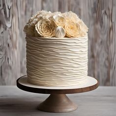 a cake with white frosting and flowers on top sitting on a wooden stand in front of a wood paneled wall