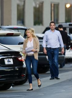 a man and woman walking down the street with cars parked on the side of the road