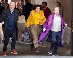 three people are walking down the street carrying suitcases and one is wearing a yellow coat