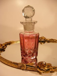 a pink perfume bottle sitting on top of a glass tray with gold trimmings