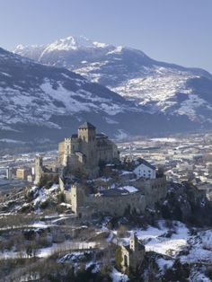 an old castle sits on top of a snowy hill with mountains in the back ground