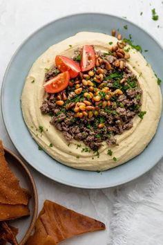 hummus with tomatoes, beans and herbs on a blue plate next to pita chips