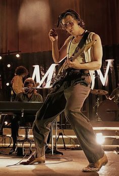 a man standing on top of a stage while holding a guitar in his right hand