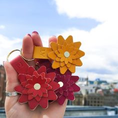 a hand holding three different colored flowers on top of each other with the city in the background