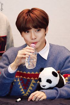 a person sitting at a table with a stuffed panda bear in front of him drinking water