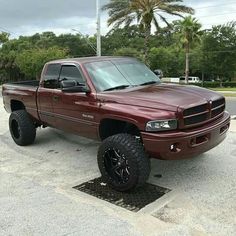 a maroon truck parked in a parking lot next to trees and palm trees on a cloudy day