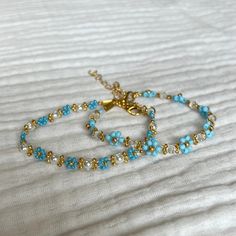 two bracelets with blue beads and gold accents on a white sheet, one is laying down