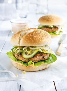 two burgers with lettuce, cucumber and mayonnaise on them