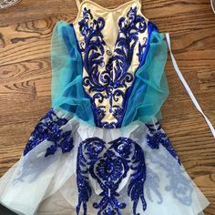 a dress made out of tulle with blue and white designs on the front, sitting on a wooden floor