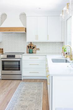 a kitchen with white cabinets and wood flooring is pictured in this image, there is a rug on the floor next to the stove