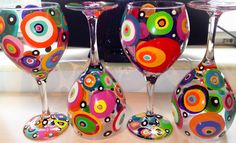 four wine glasses with colorful designs on them sitting on a counter top next to a window