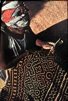 a woman sitting on the ground working on an intricately designed piece of cloth with scissors