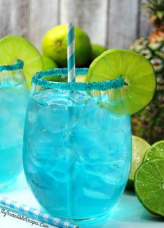 two glasses filled with blue liquid and limes next to each other on a table