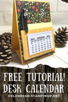 a desk calendar sitting on top of a wooden table next to pine cones and a pen