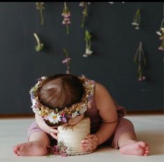 a baby is sitting on the floor with a cake in front of her and wearing a flower crown