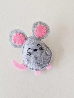 a gray and pink mouse brooch sitting on top of a white surface with its eyes closed