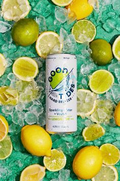 a can of soda surrounded by lemons, limes and ice on a green surface