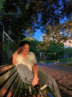 a woman sitting on top of a wooden bench next to a park filled with trees